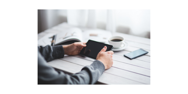 Ihminen pitää tablettia käsissään pöydän ääressä Ihminen pitää tablettia käsissään pöydän ääressä